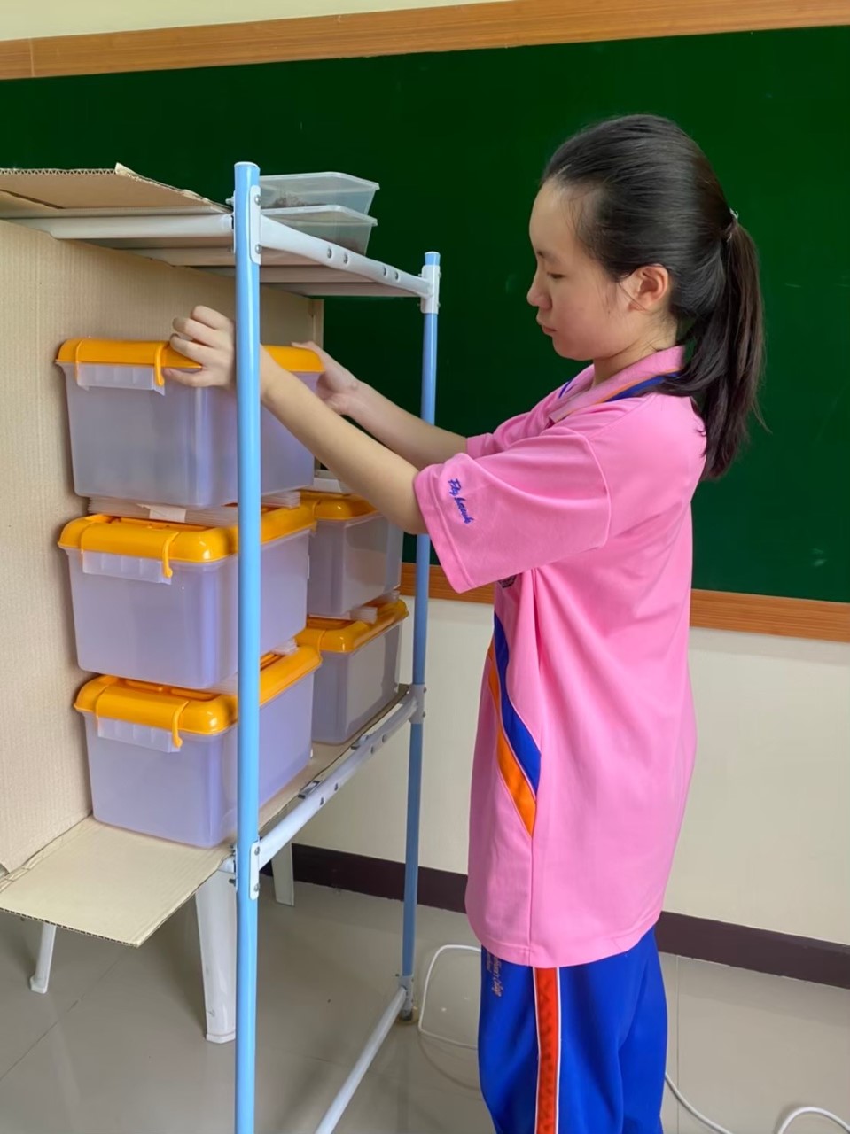 a girl wearing a pink shirt arranges a stack of plastic bins on a shelf